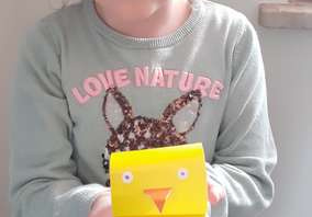 Uśmiechnięta dziewczynka trzyma kurczaczka wykonanego z żółtego papieru